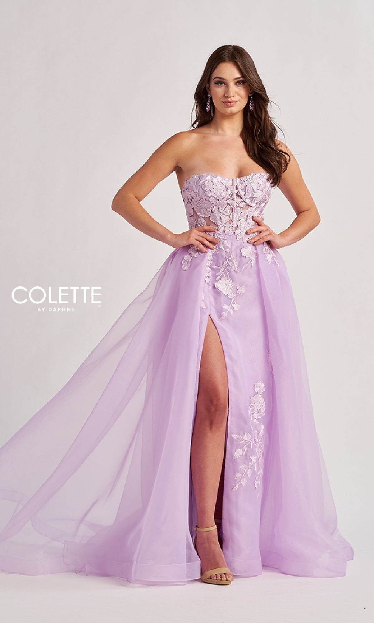 A woman in the Long Prom Dress: Colette CL8660, a strapless lavender ball gown with a sheer lace bodice, floral embroidered A-line skirt, and thigh-high slit, stands on a neutral background.